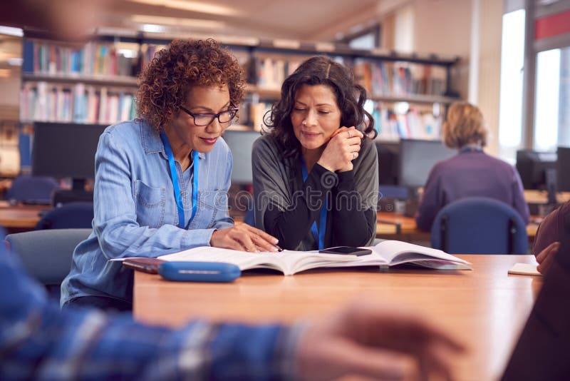 Profesora con estudiante adulta madura sentada en la mesa trabajando en la biblioteca universitaria fotografía de archivo libre de regalías