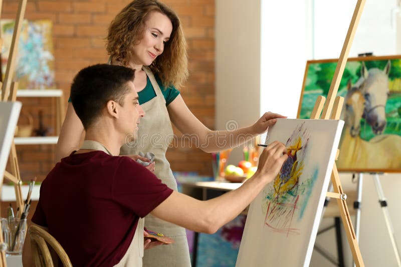 Professeur féminin aidant son étudiant pendant les classes à l'école des peintres photographie stock libre de droits Professeur féminin aidant son étudiant pendant les classes à l'école des peintres photographie stock libre de droits