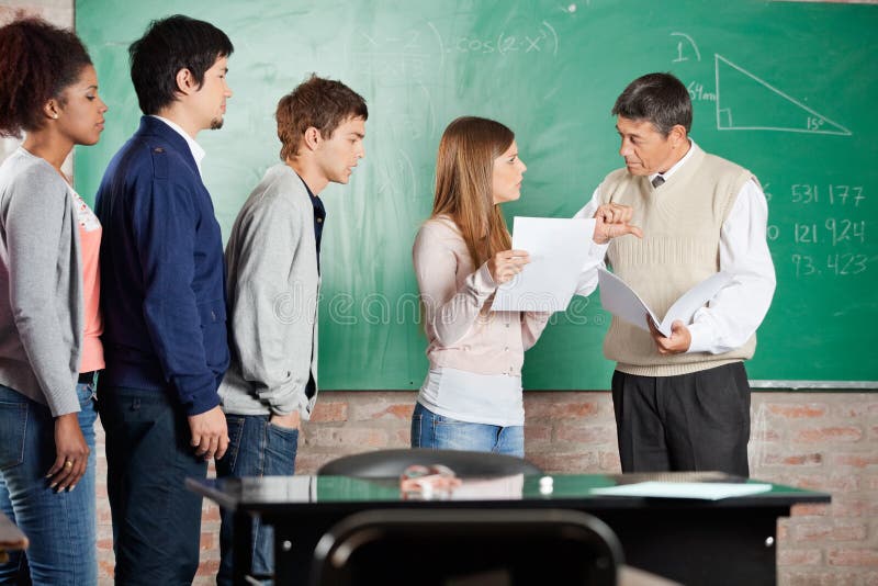 Mature teacher gesturing thumbsdown while looking at female student in classroom. Mature teacher gesturing thumbsdown while looking at female student in classroom