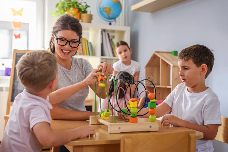 Professeur préscolaire avec des enfants jouant avec les jouets didactiques colorés au jardin d'enfants photographie stock Professeur préscolaire avec des enfants jouant avec les jouets didactiques colorés au jardin d'enfants photographie stock