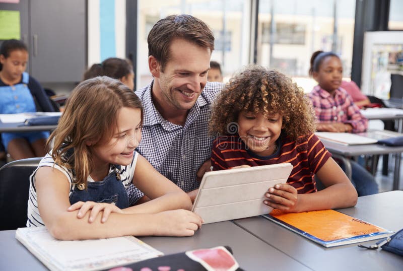 Professeur à l'aide du comprimé avec deux élèves dans la classe d'école photos libres de droits Professeur à l'aide du comprimé avec deux élèves dans la classe d'école photos libres de droits