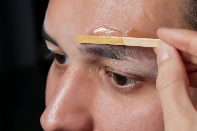 Professional barber doing threading procedure and correcting shape of eyebrows to young male client with tweezer in stock image
