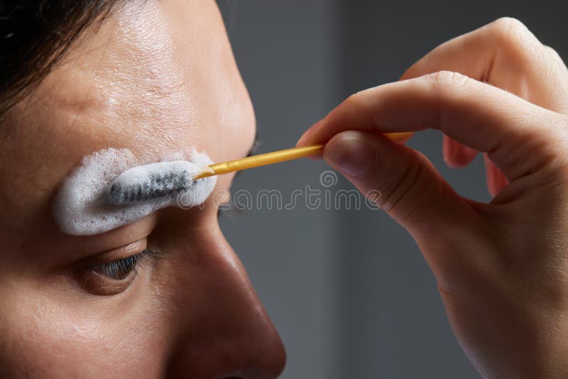 Professional barber doing threading procedure and correcting shape of eyebrows to young male client with tweezer in stock image