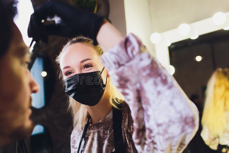 Professional barber in white shirt doing threading procedure and correcting shape of eyebrows to young male client stock image