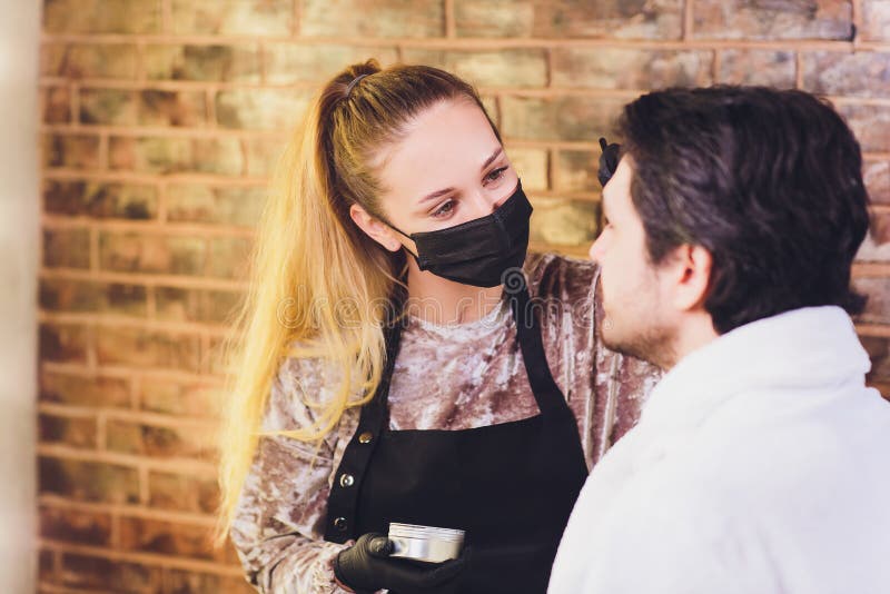 Professional barber in white shirt doing threading procedure and correcting shape of eyebrows to young male client royalty free stock photos