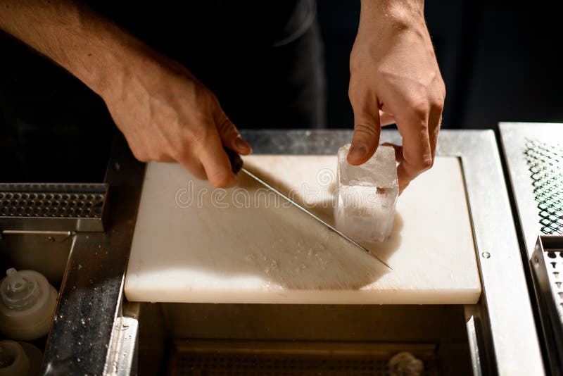 Professional Bartender Cutting Ice with a Knife on the White Board on