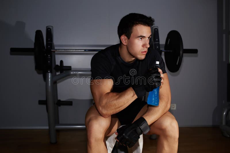 Professional bodybuilder holding bottle of energy drink and looking away