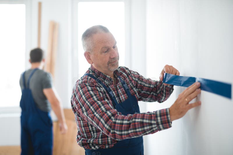 Professional builder puts a tape on an wall before painting it royalty free stock image