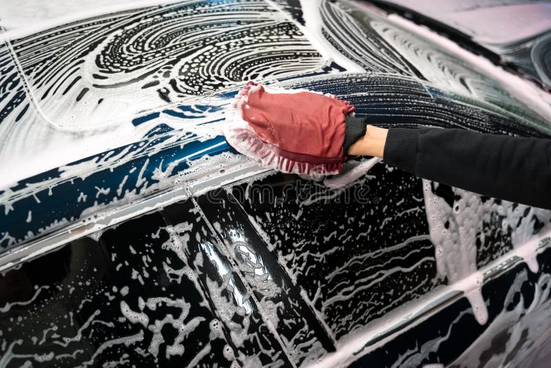 Professional car wash. Detailing worker washes the vehicle body with foam and rag.