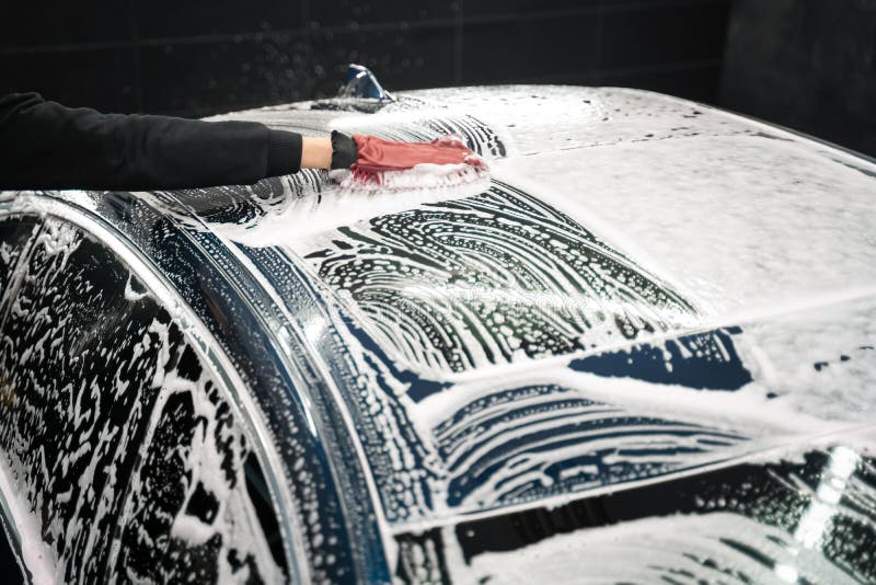 Professional car wash. Detailing worker washes the vehicle body with foam and rag.