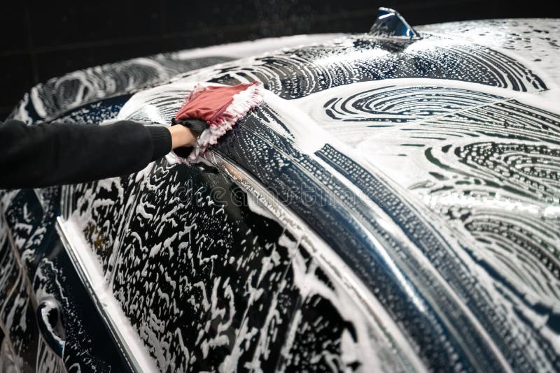 Professional car wash. Detailing worker washes the vehicle body with foam and rag.