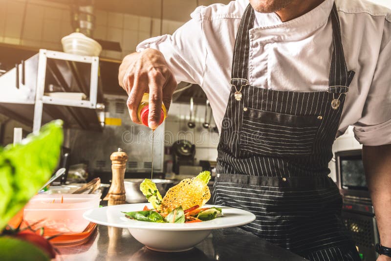 Professional chef cooking in the kitchen restaurant at the hotel, preparing dinner. A cook in an apron makes a salad of