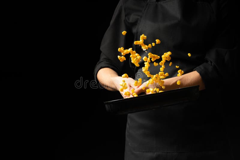 Professional cook. Chef is preparing a dish with corn in a pan. on a black background. menu, recipe book, healthy food, restaurant