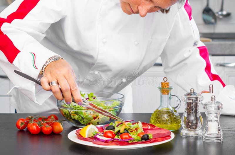 Professional cook prepares a plate with salami and fresh salad stock photo