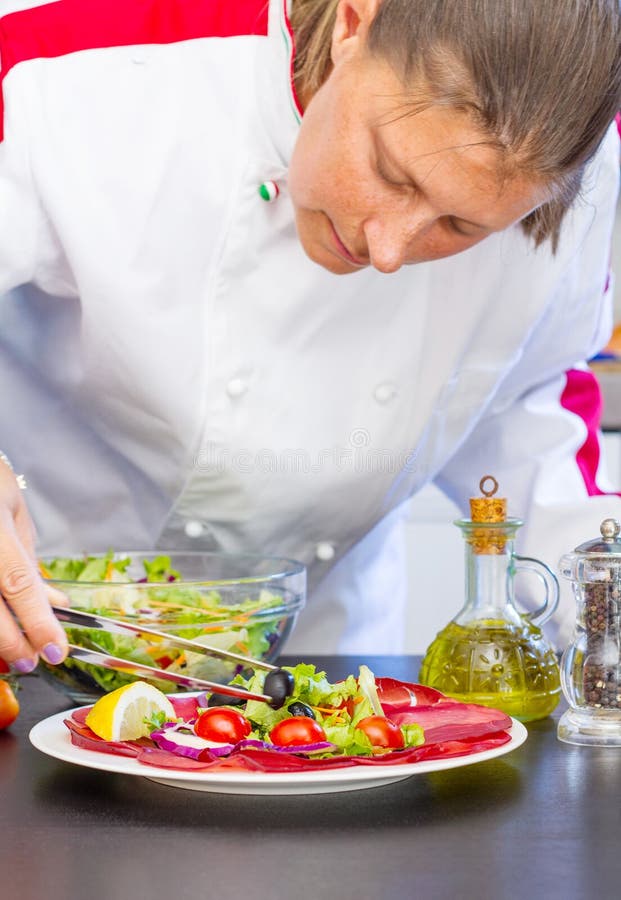 Professional cook prepares a plate with salami and fresh salad royalty free stock images