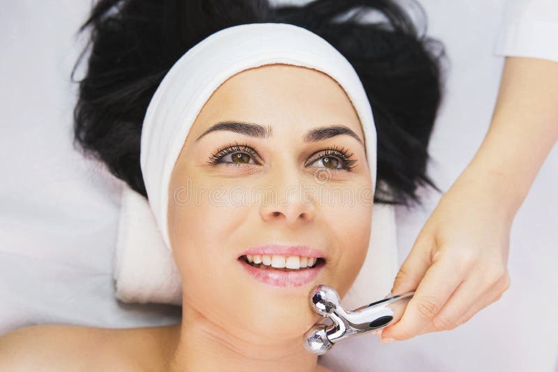 Professional Cosmetologist Using Facial Roller Massage Instrument To Make Rejuvenation Face