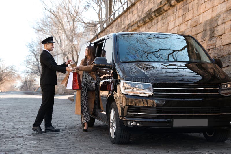 Professional driver helping woman with bags to get out of car. Chauffeur service royalty free stock photography Professional driver helping woman with bags to get out of car. Chauffeur service royalty free stock photography