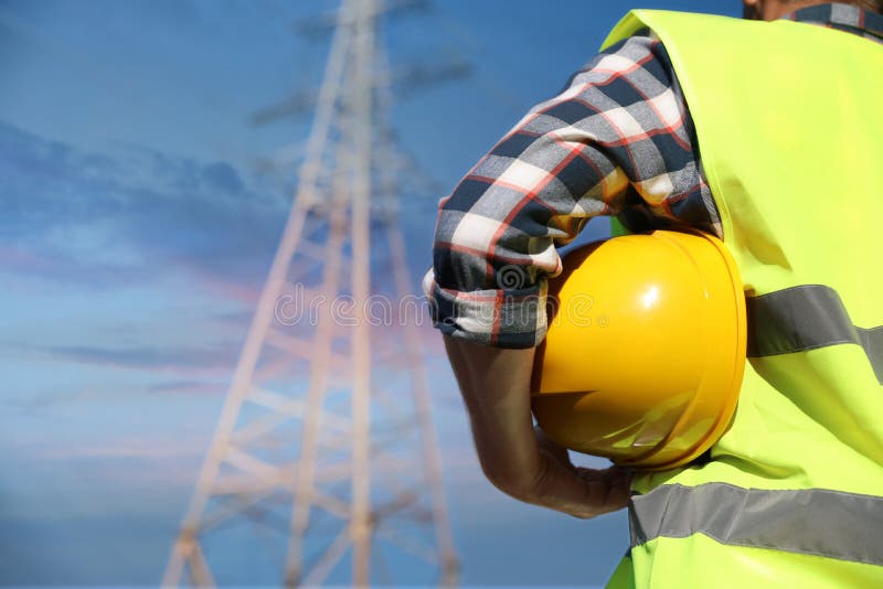 Professional electrician with helmet near high voltage tower, closeup