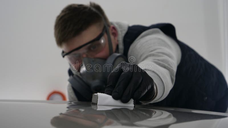 A professional male boy master of ceramics of a car puts ceramics on a car using a fiber sponge rag in a puller, safety goggle