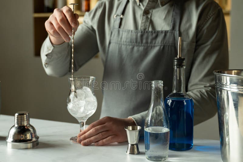 Professional Man Bartender Stirring Ice in the Glass on the Bar Counter