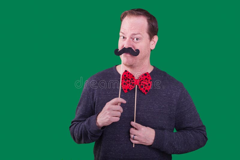 Male model holding fake mustache to face red bowtie photo booth prop captured a green screen background stock photos Male model holding fake mustache to face red bowtie photo booth prop captured a green screen background stock photos