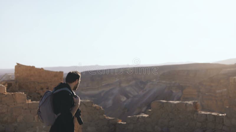 Professional photographer explores ancient ruins. European man with camera and backpack near mountain view. Israel 4K.
