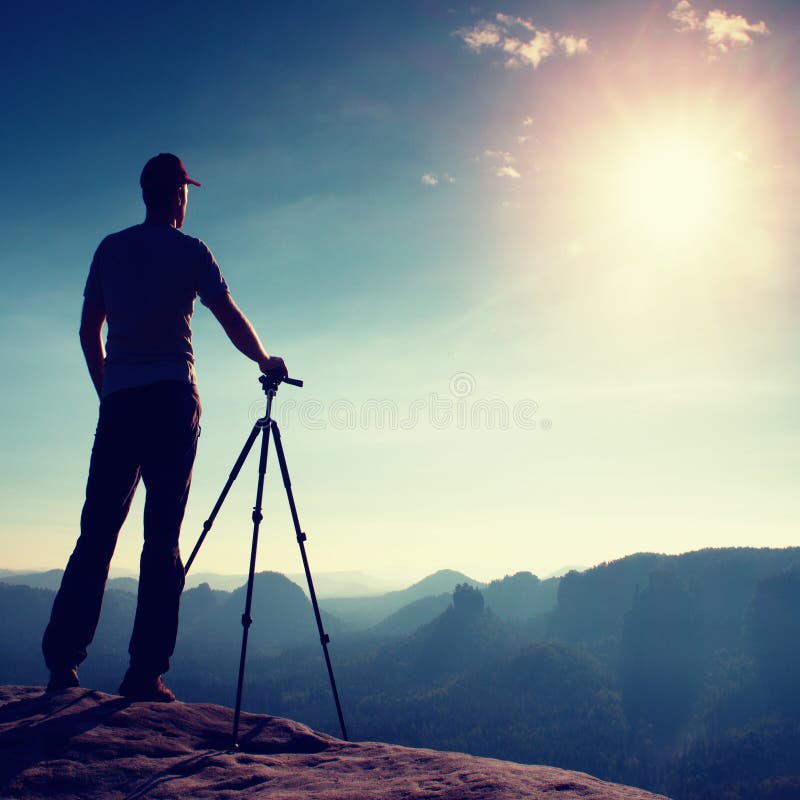 Professional photographer stay with tripod on cliff and thinking. Dreamy fogy landscape, blue misty sunrise in a beautiful valley stock photography Professional photographer stay with tripod on cliff and thinking. Dreamy fogy landscape, blue misty sunrise in a beautiful valley stock photography