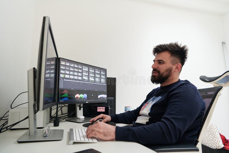 Professional video editor enhancing digital footage using specialized software. Expert videographer in home office workspace editing on dual screen workstation computer desktop workplace