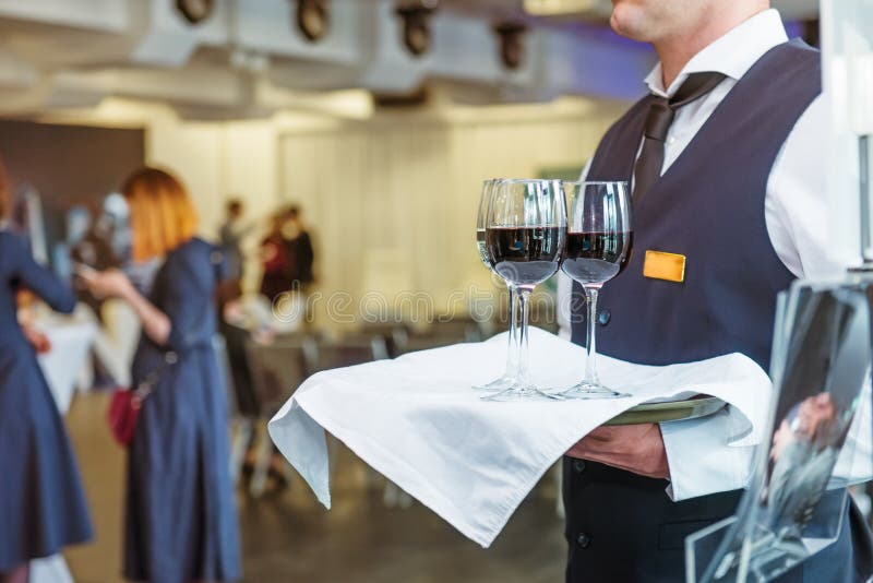 Professional waiter in uniform holding a tray with glasses of vine at business event. Catering or celebration concept. Service at