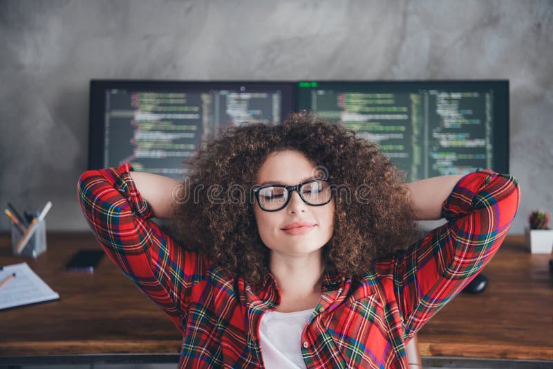 Young professional female programmer relaxing in a casual office with curly hair, coding screens in background stock images