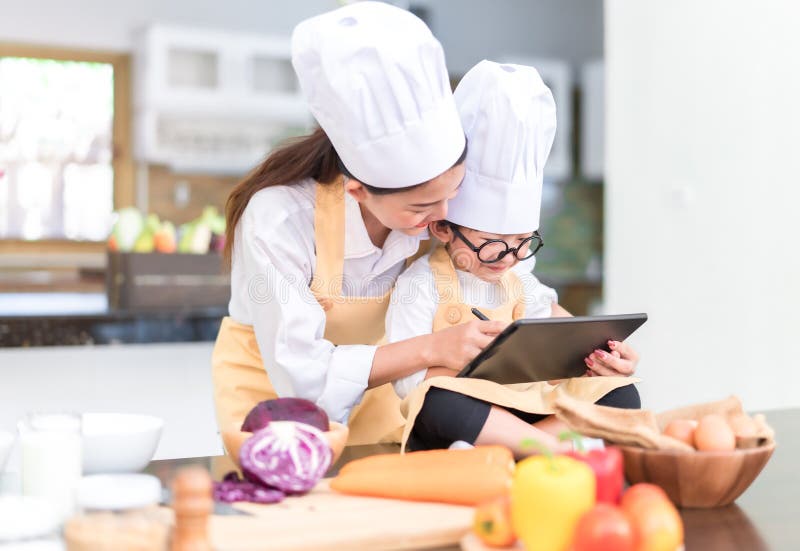 Professioneel Chef-kok Aziatisch mamma die weinig het menu van de zoonslijst het koken onderwijzen royalty-vrije stock foto Professioneel Chef-kok Aziatisch mamma die weinig het menu van de zoonslijst het koken onderwijzen royalty-vrije stock foto