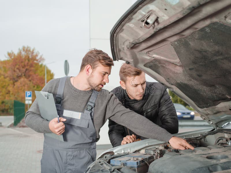 Professionele autowerktuigkundige die iets in de open kap buiten tonen aan cliënt stock foto Professionele autowerktuigkundige die iets in de open kap buiten tonen aan cliënt stock foto