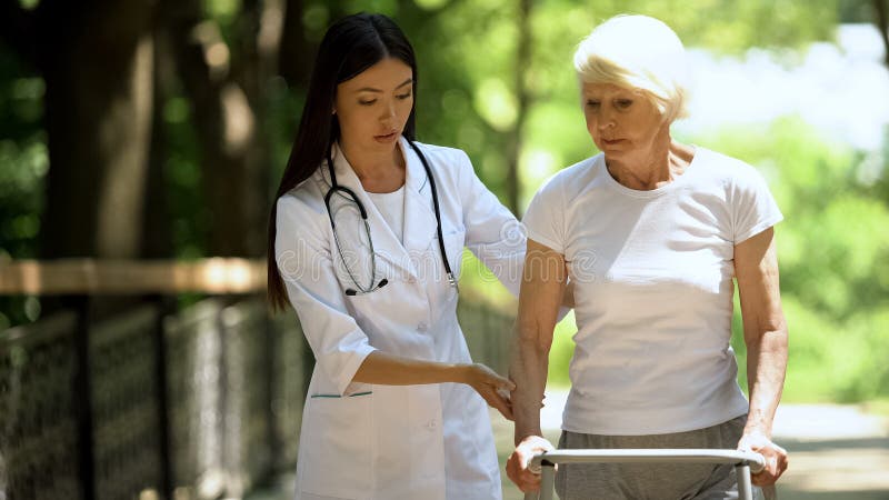 Professional female nurse supporting old women moving in park with walking frame, stock photo. Professional female nurse supporting old women moving in park with walking frame, stock photo