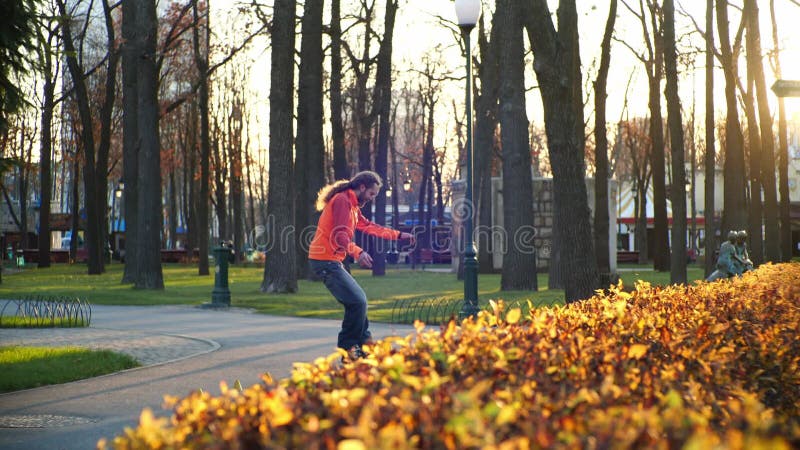 Professionell rullskridskog på hösten i en stadspark i soligt väder. en man med skägg gör olika rullar arkivfilmer
