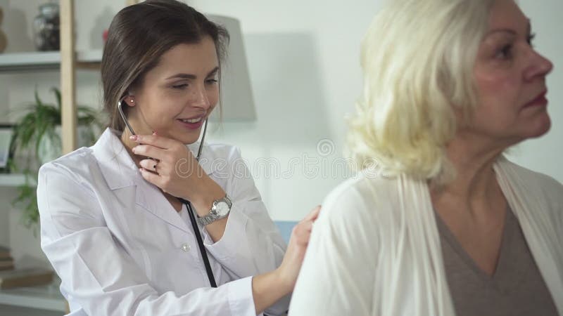 Professionista che per mezzo dello stetoscopio e visitando donna senior a casa