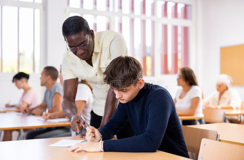 Professor afro-americano ajudando estudante a resolver a tarefa durante a aula imagem de stock royalty free