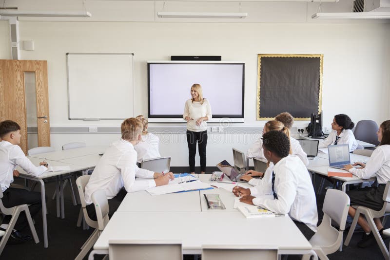 Professor alto fêmea Standing Next To Whiteboard interativo e lição de ensino aos alunos que vestem o uniforme
