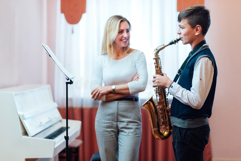 Cheerful teacher with student boy learning saxophone lessons at music school. Cheerful teacher with student boy learning saxophone lessons at music school