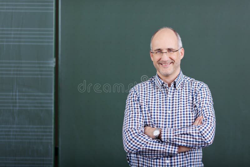 Professor With Arms Crossed Standing Against Chalkboard stock photo