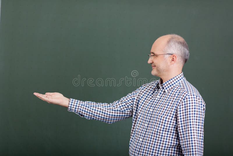 Professor Displaying Invisible Product Against Chalkboard royalty free stock photography