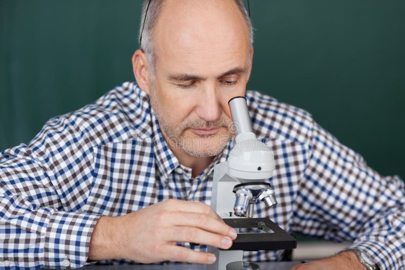 Professor Looking Through Microscope In Science Class stock images