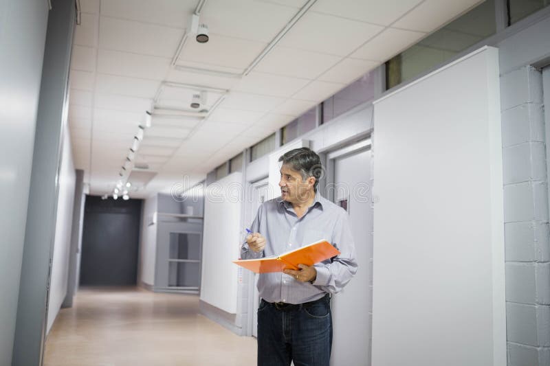Man inspecting office corridor with paneled walls holding orange folder and pen near ceiling lights royalty free stock photos