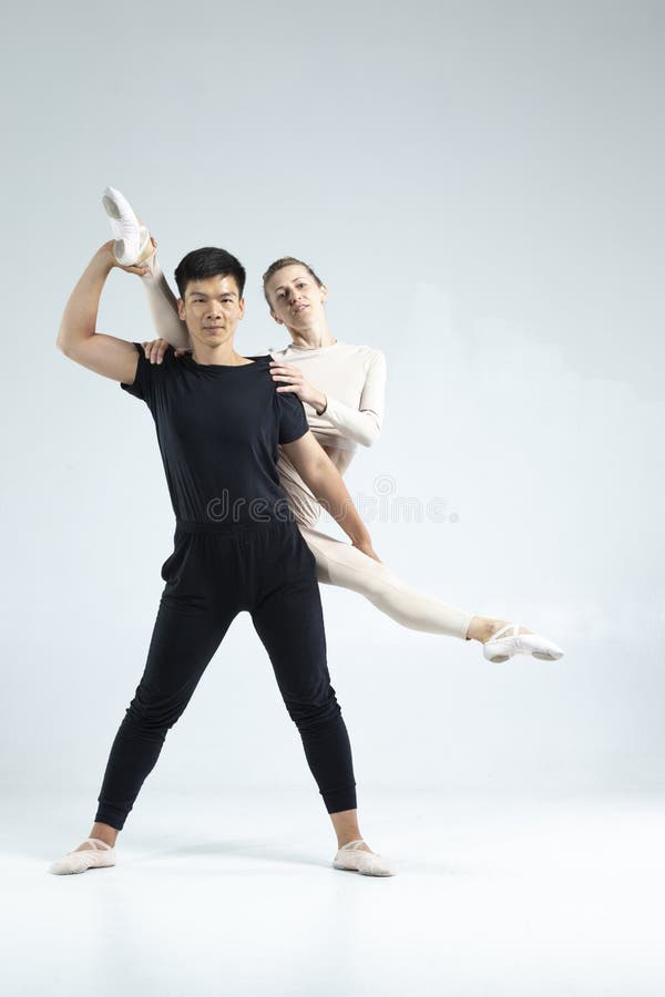 Proffs- och idrottsligt par av asiatisk man och kaukasisk kvinna som opererar som balettdansare över grått i studio under upptag a arkivfoto