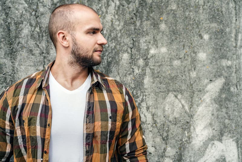 Profil du jeune type barbu audacieux beau se tenant dehors contre le mur moderne gris de grenier regardant de côté avec le visage image stock Profil du jeune type barbu audacieux beau se tenant dehors contre le mur moderne gris de grenier regardant de côté avec le visage image stock