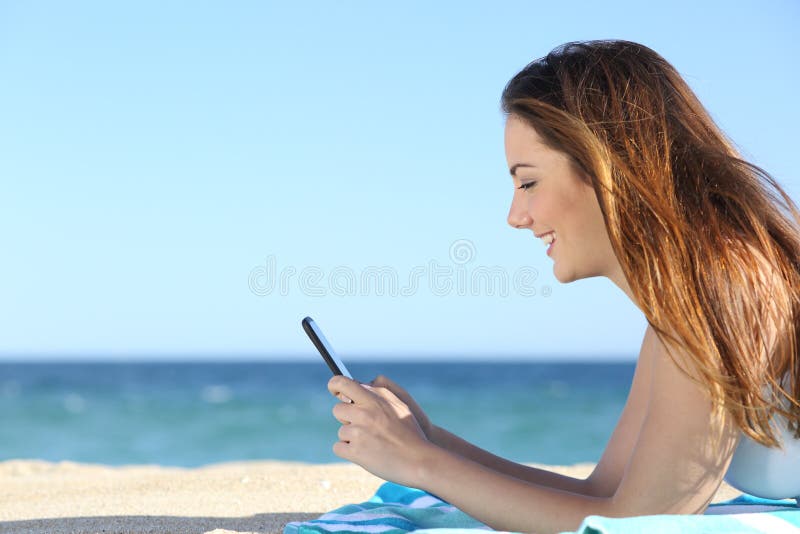 Profil einer Frau, die in einem intelligenten Telefon auf dem Strand simst stockbild Profil einer Frau, die in einem intelligenten Telefon auf dem Strand simst stockbild