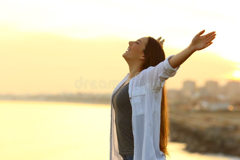 Side view portrait of a woman breathing deep fresh air outstretching arms at sunset with the city in the background. Side view portrait of a woman breathing deep fresh air outstretching arms at sunset with the city in the background