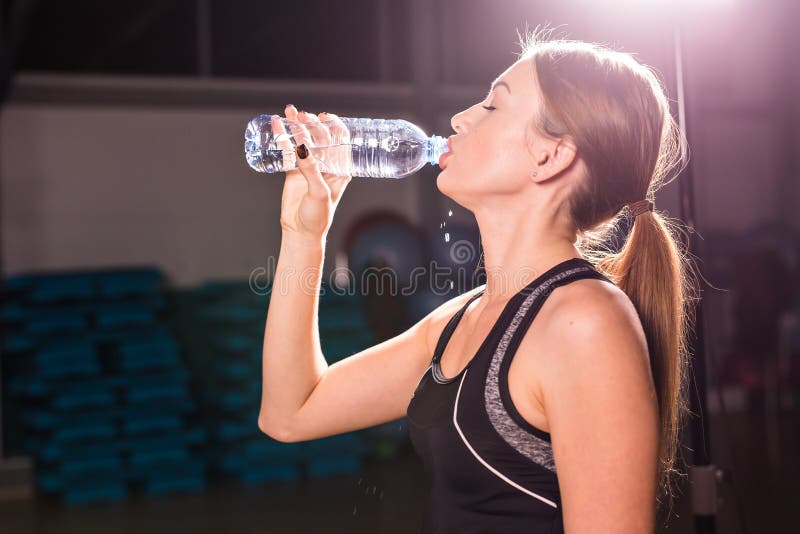 Profile of beautiful woman going to drink some water from plastic bottle after workout