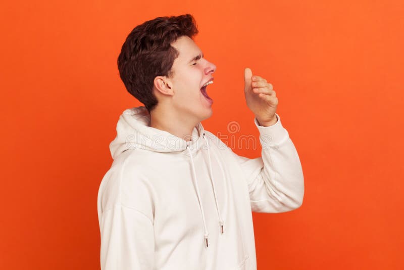 Profile of bored young man in casual style sweatshirt with hood yawning, sleepy teenager exhausted of early awakenings, laziness