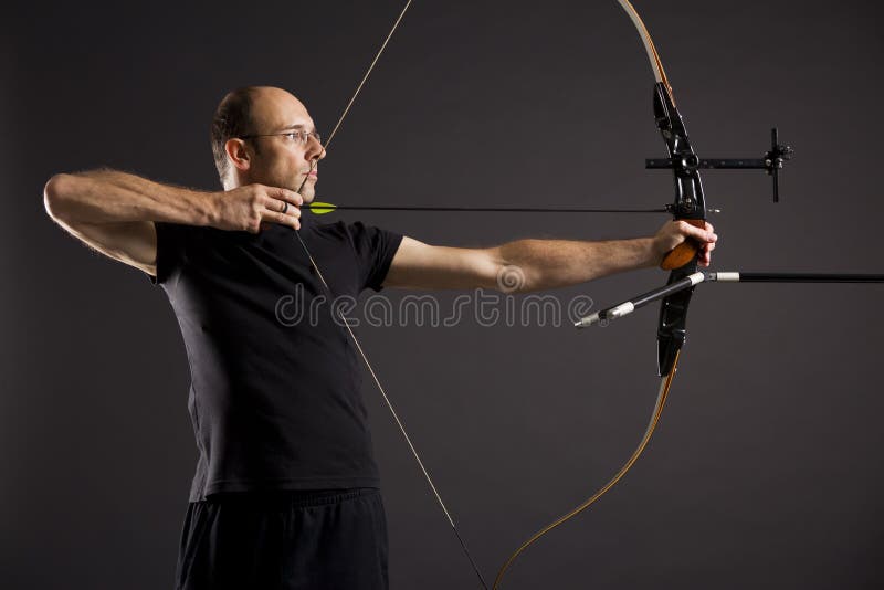 Retrato jugador de pelota en negro sobre un fondo negro apuntar arco a flecha, página concentrarse sobre el ojos.