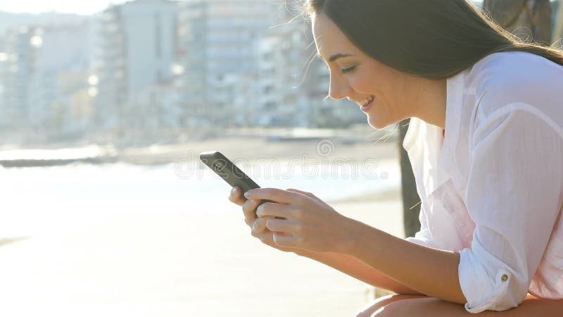 Profile of a girl using smart phone in the coast